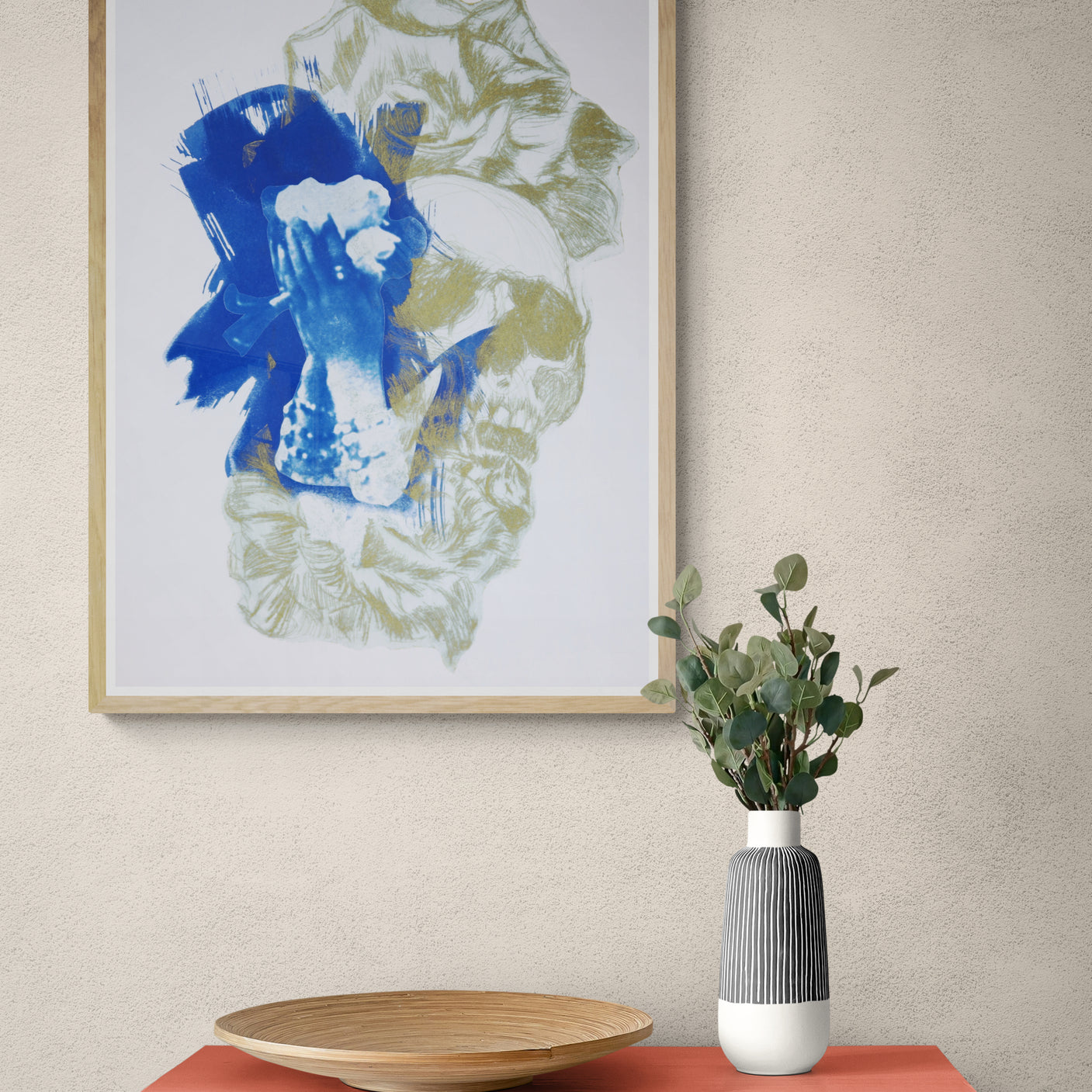 Œuvre de la collection Memoria encadrée, cyanotype et gravure sur papier, motif de fleurs, de crâne et de mains sur le visage, présentée en intérieur.