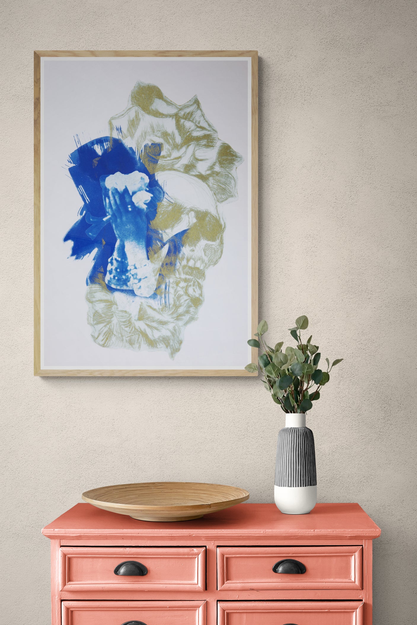 Œuvre de la collection Memoria encadrée, cyanotype et gravure sur papier, motif de fleurs, de crâne et de mains sur le visage, présentée en intérieur.