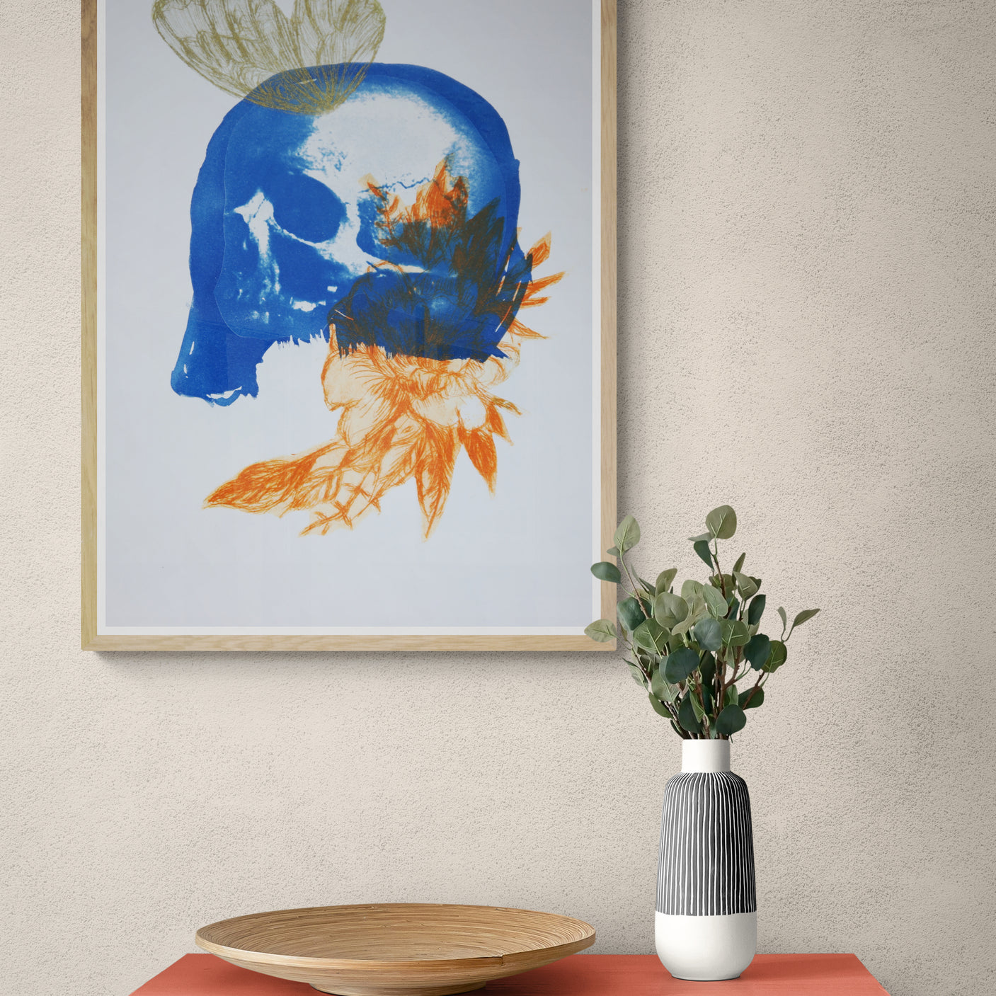 Œuvre de la collection Memoria encadrée, cyanotype et gravure sur papier, motif de papillon, de crâne et de fleur orange, présentée en intérieur.