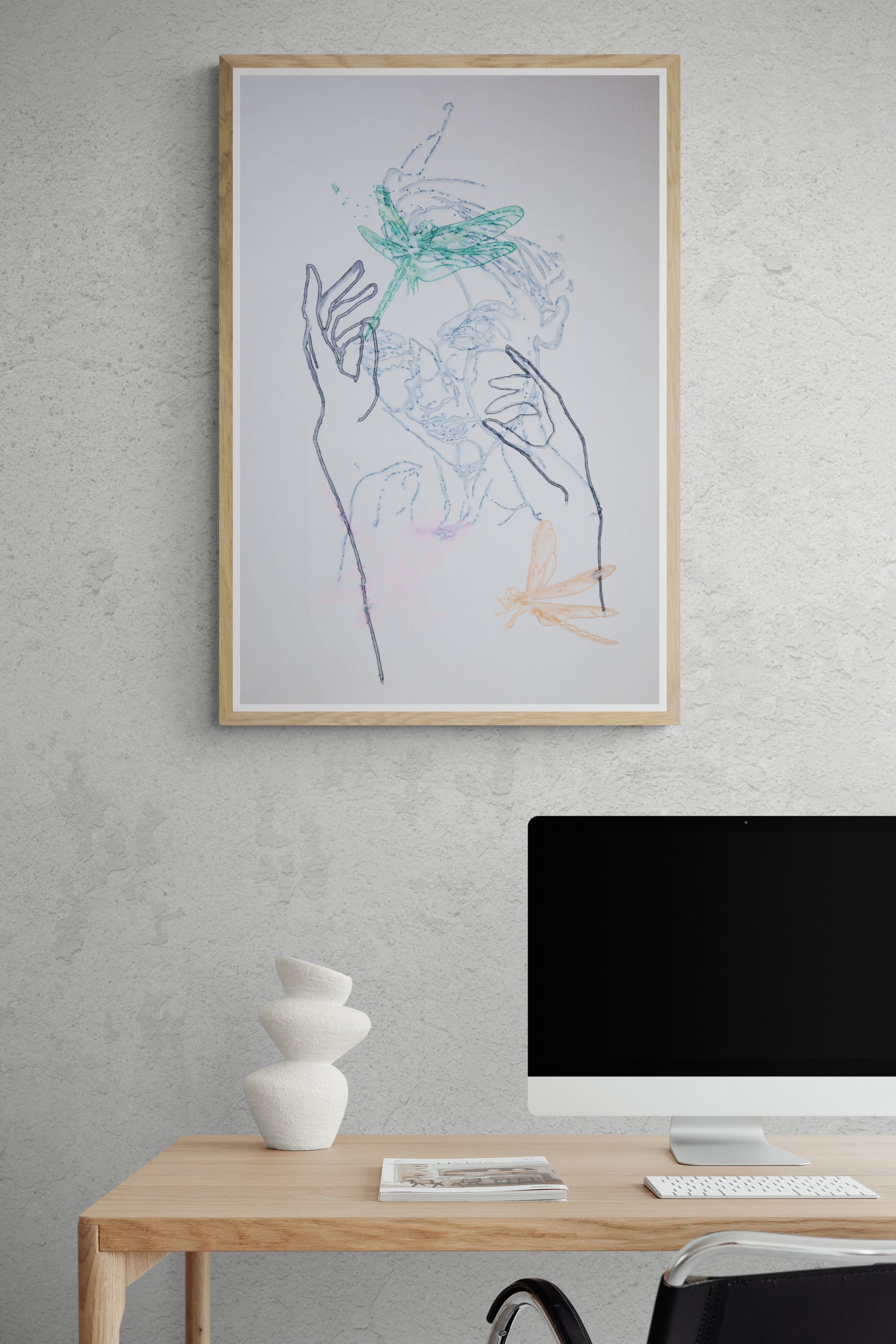 Œuvre de la collection Métamorphe encadrée, aquarelle sur papier, motif de libellules, de visage et de mains, aux teintes bleu, vert et rose, présentée en intérieur.